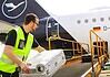 Loader places suitcases on the conveyor belt for loading a Lufthansa Airbus