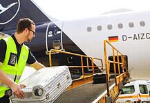 Loader places suitcases on the conveyor belt for loading a Lufthansa Airbus